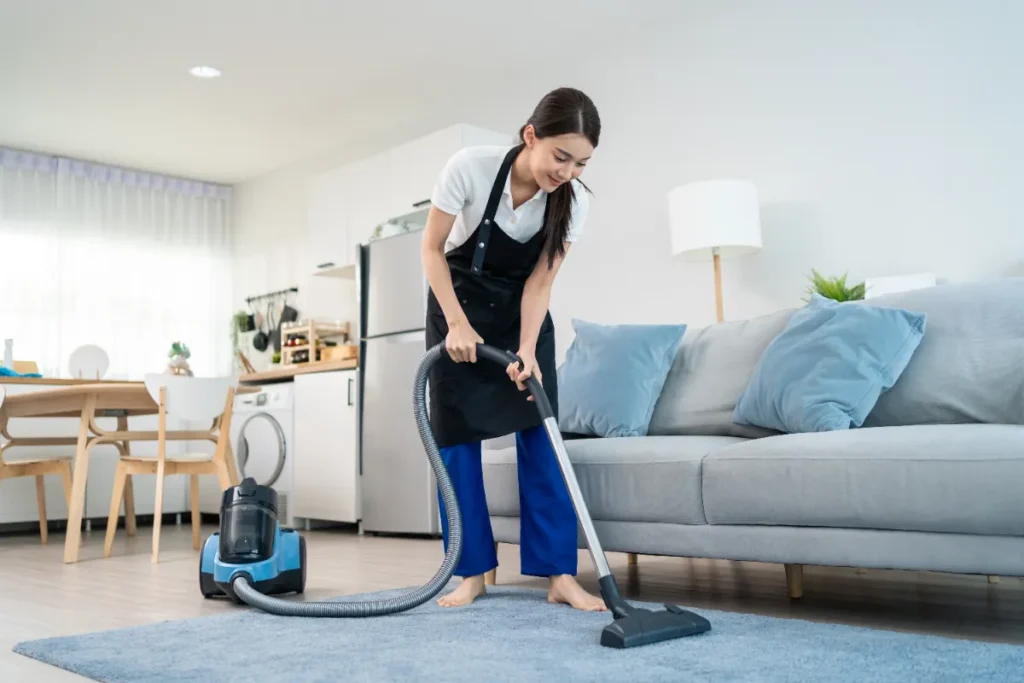 Professional cleaner vacuuming a living room during a weekly routine cleaning service.