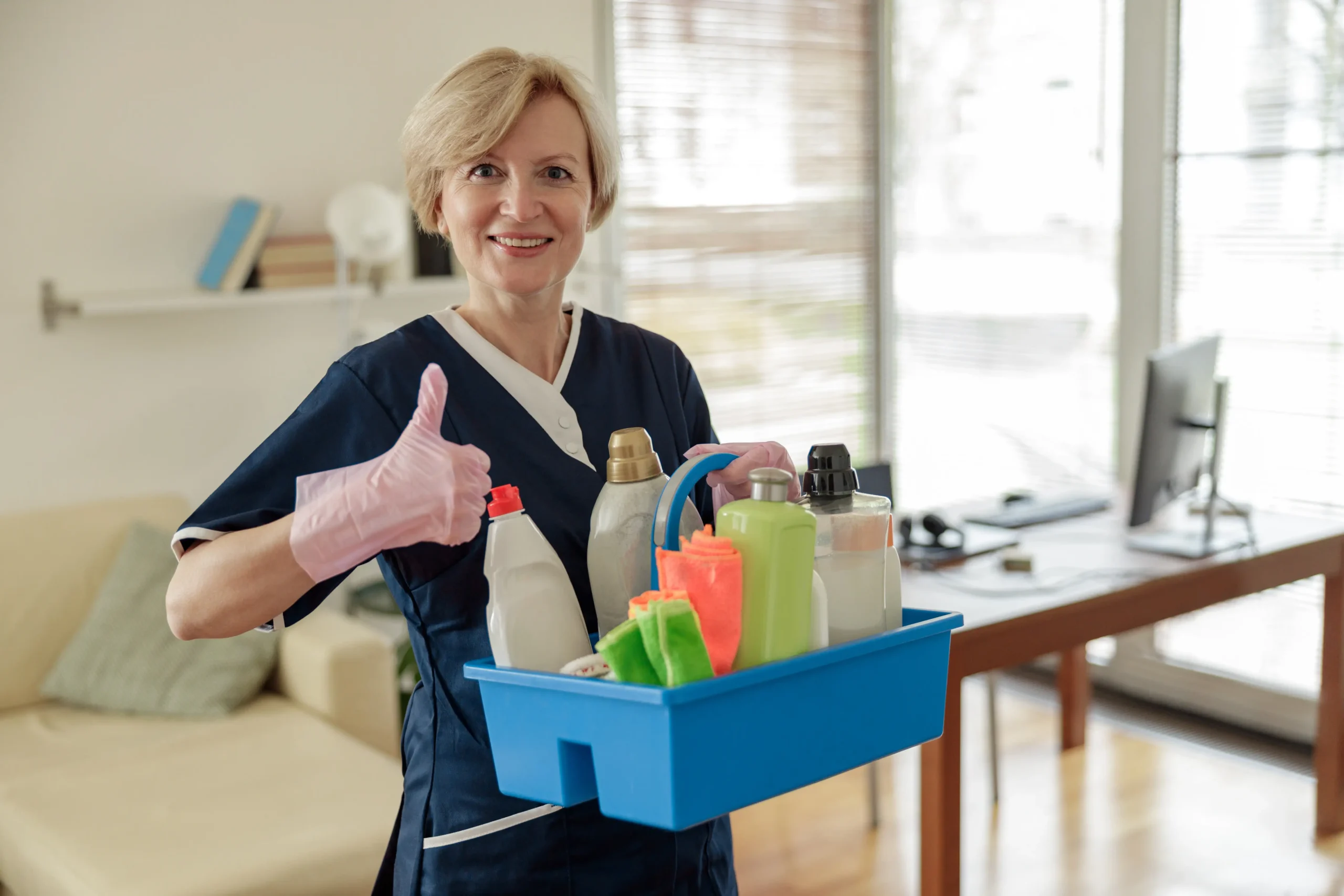 A smiling mature woman carrying a cleaning items and giving a thumbs up