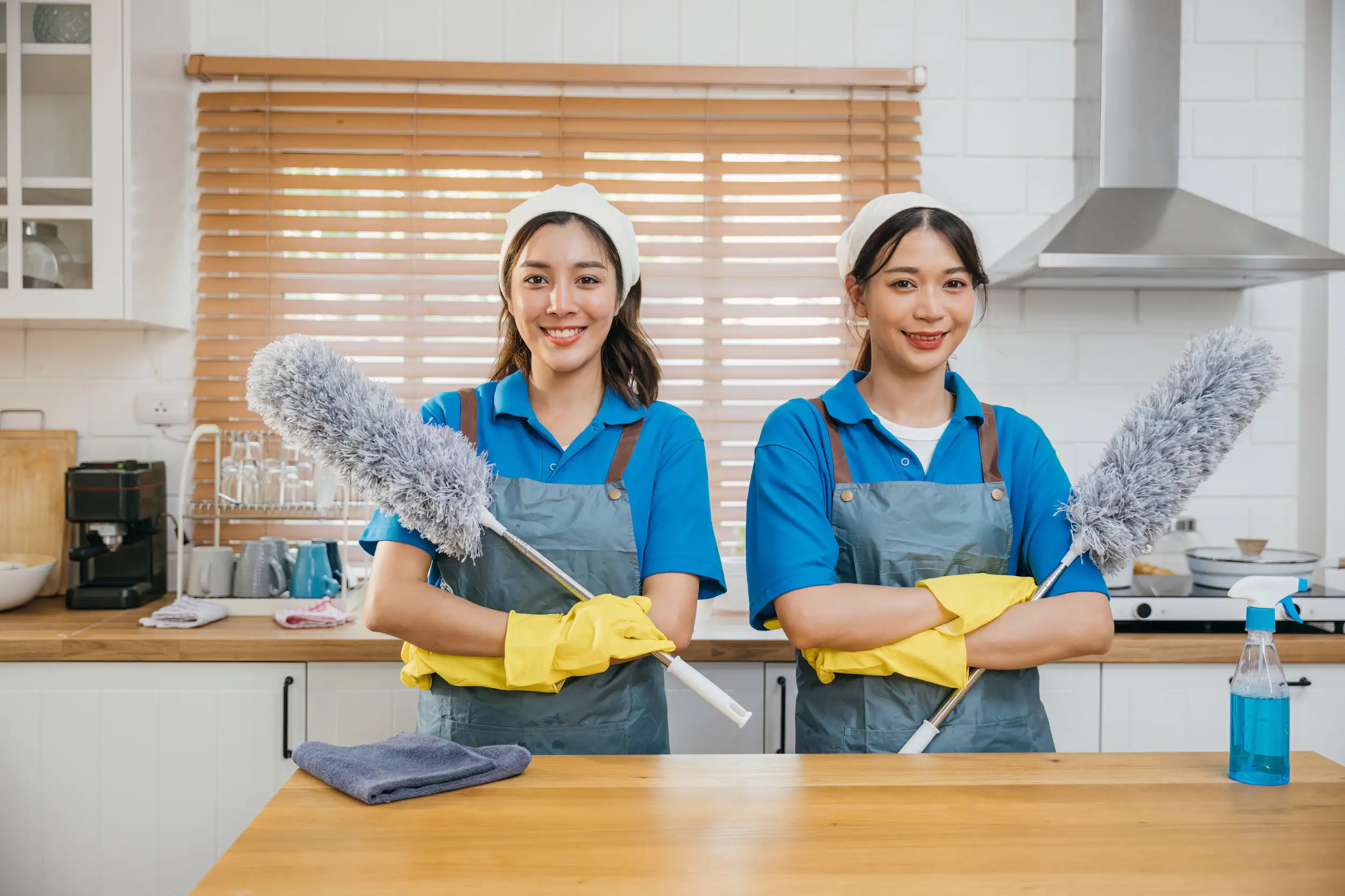 Two smiling cleaning crew holding a feather duster ready to clean the house.